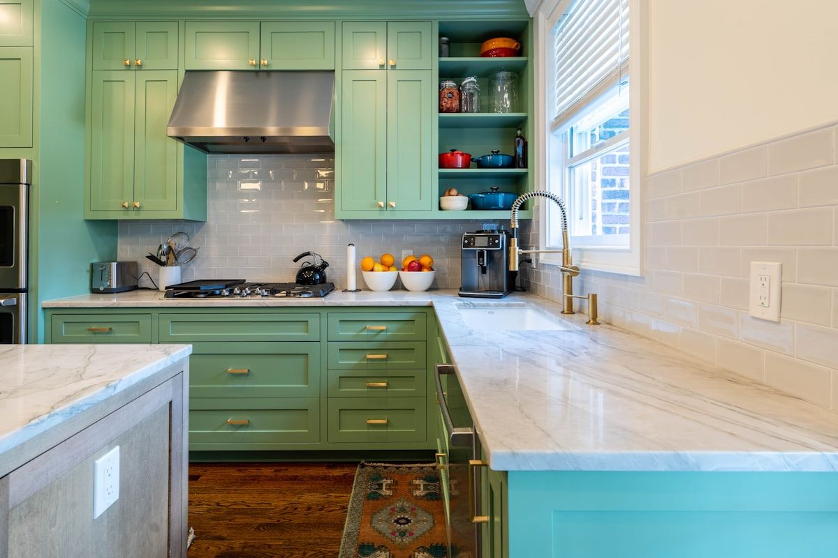 Green kitchen cabinets with marble counters and a white tile backsplash.